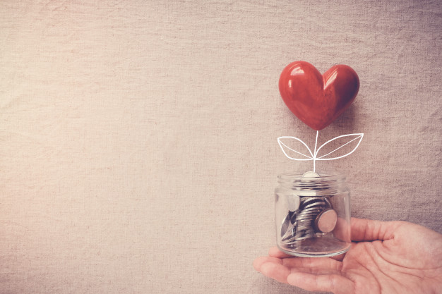 Mão segurando uma jarra com moedas e um coração, representando uma doação
